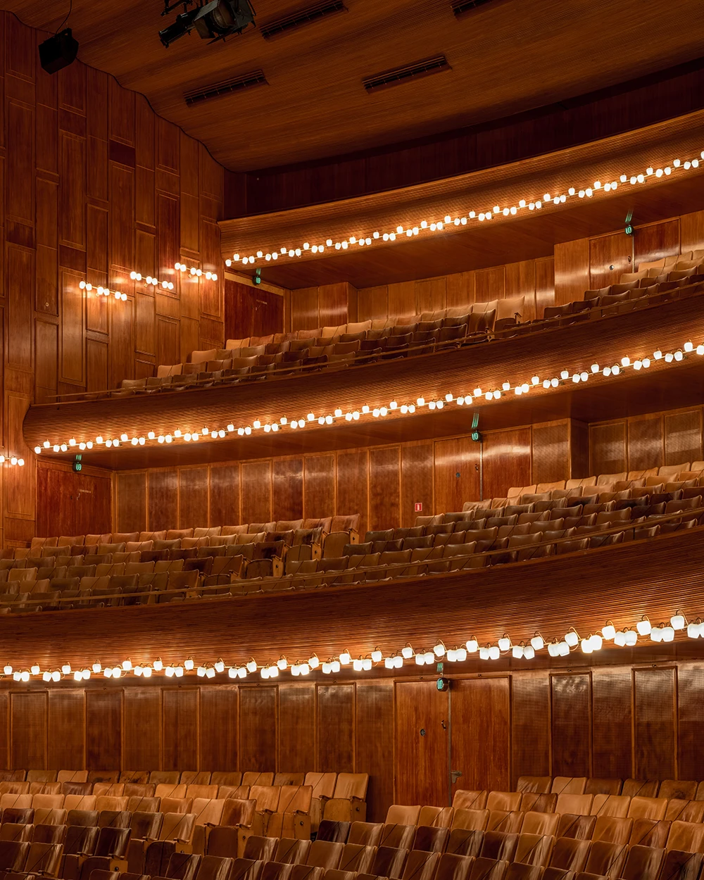 PH 2/1 Wall Lamps line the balconies of a concert hall with warm wood panelling and rows of seats. © 2026 Louis Poulsen.
