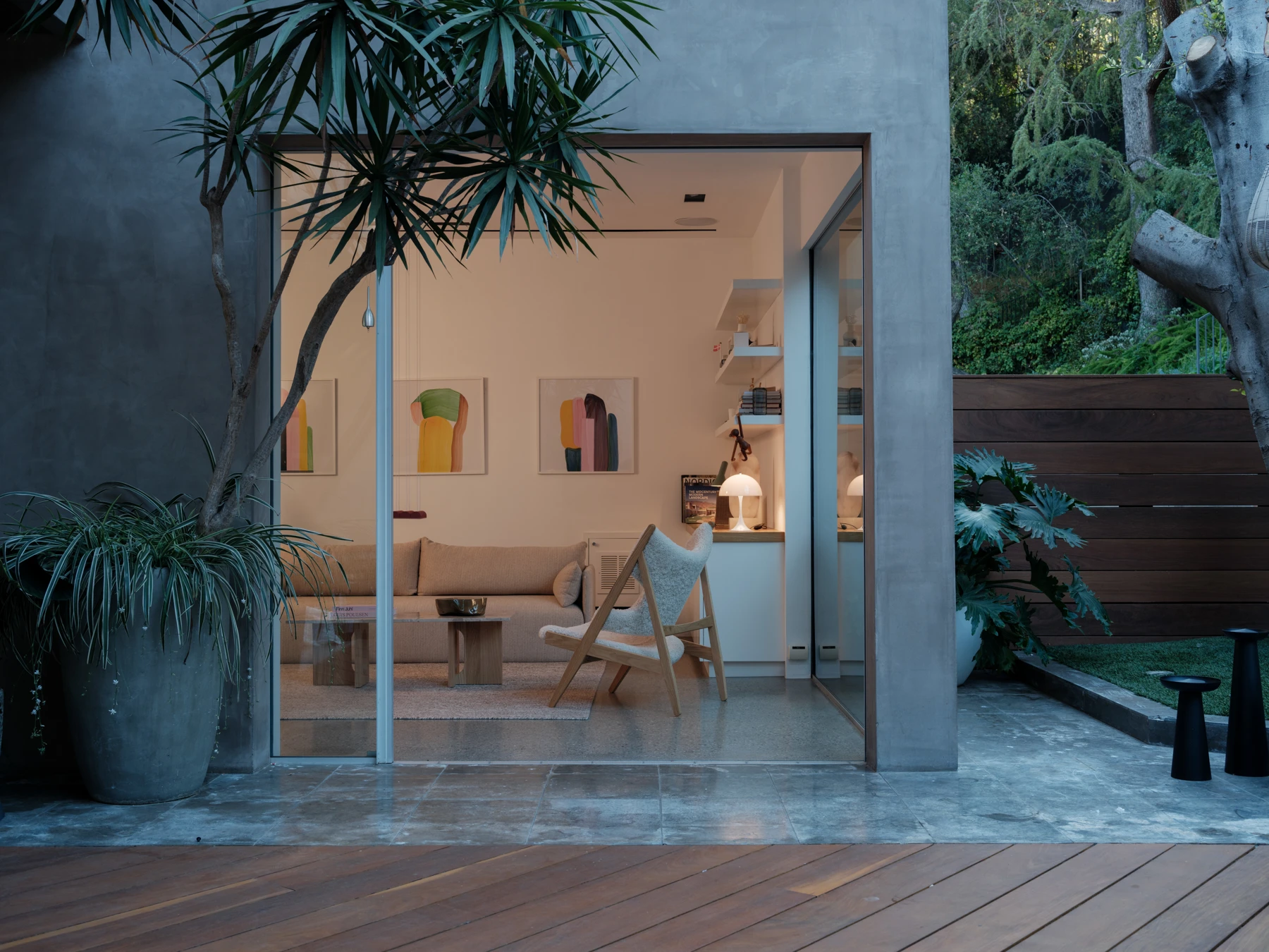 A white Panthella 250 Table Lamp glows in a modern living room opening onto a leafy garden. © 2026 Louis Poulsen.