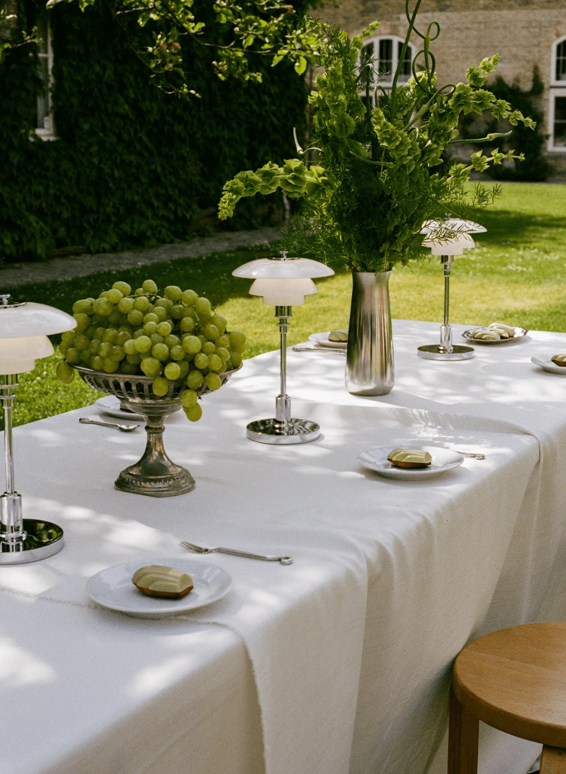 La lampe portable PH 2/1 en verre blanc et chrome est posée sur une table de jardin dressée, près de raisins et de feuillage. © 2026 Louis Poulsen.
