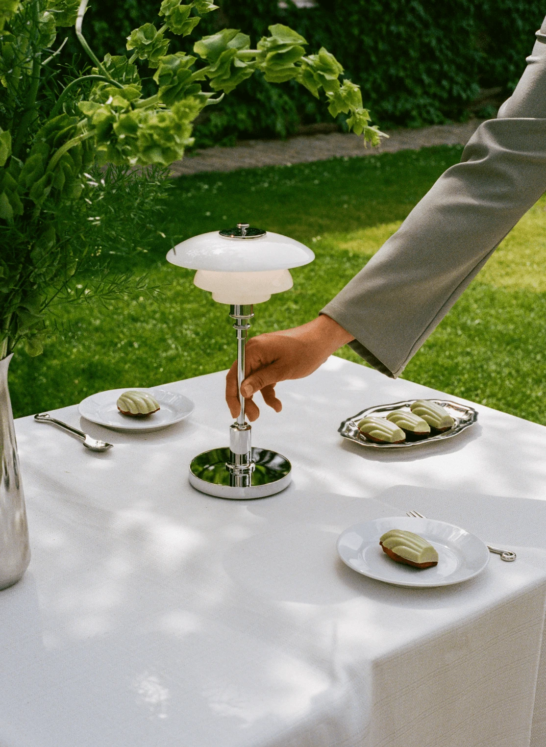 La lampe portable PH 2/1, avec ses abat-jour en verre opalin blanc, est posée sur une table de jardin qu’une main la déplace. © 2026 Louis Poulsen.