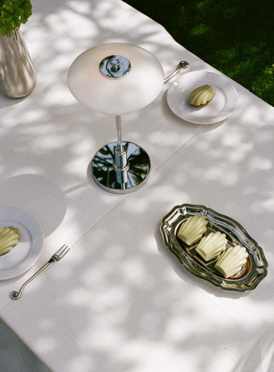 La lampe de table PH 2/2 Luna, à l’abat-jour blanc opalin et aux détails chromés, trône sur une table dressée avec des pâtisseries. © 2026 Louis Poulsen.