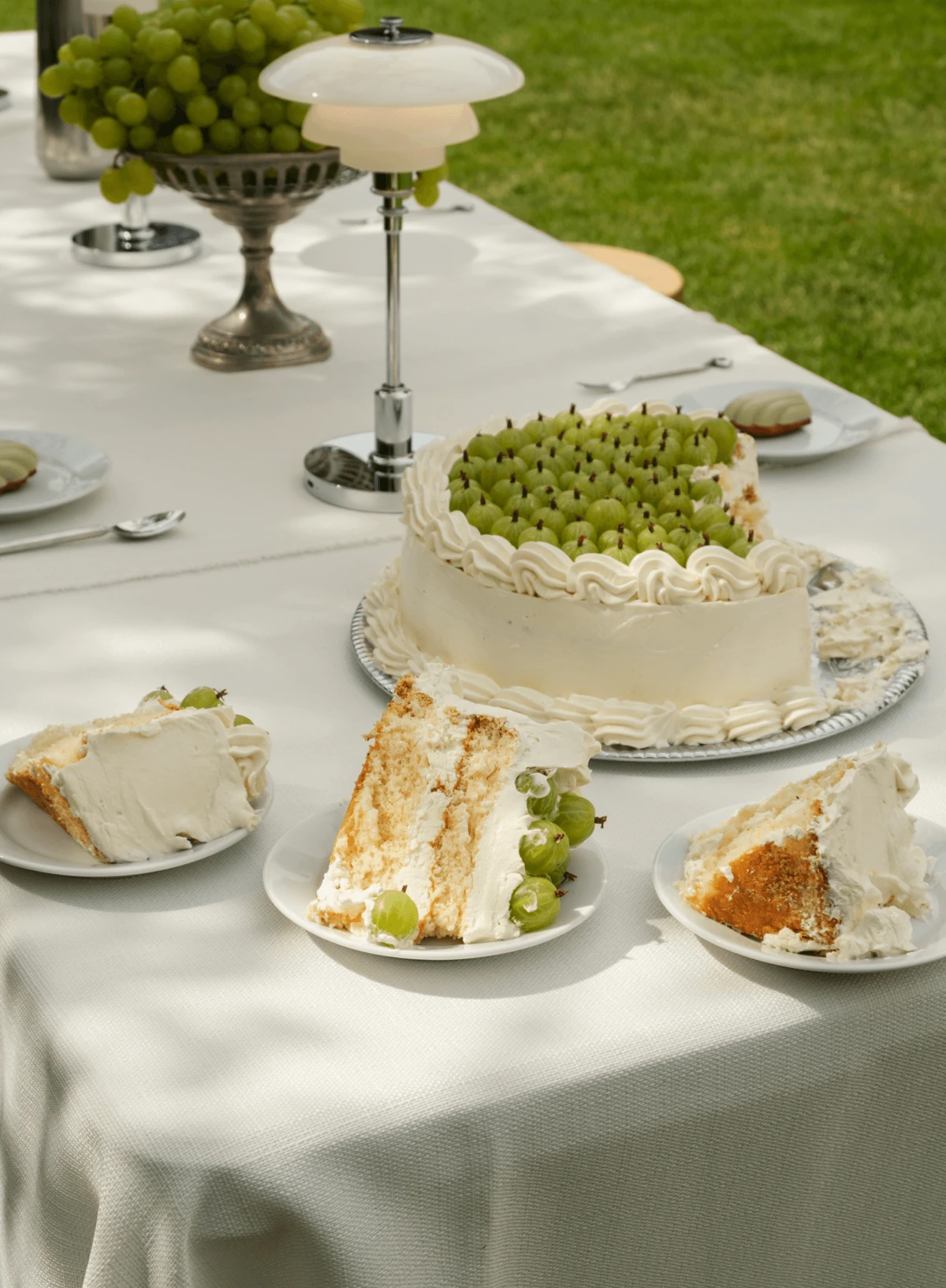 Une lampe de table PH 2/1 aux abat-jour en verre blanc et aux détails chromés se dresse près d’un gâteau sur une table de fête. © 2026 Louis Poulsen.