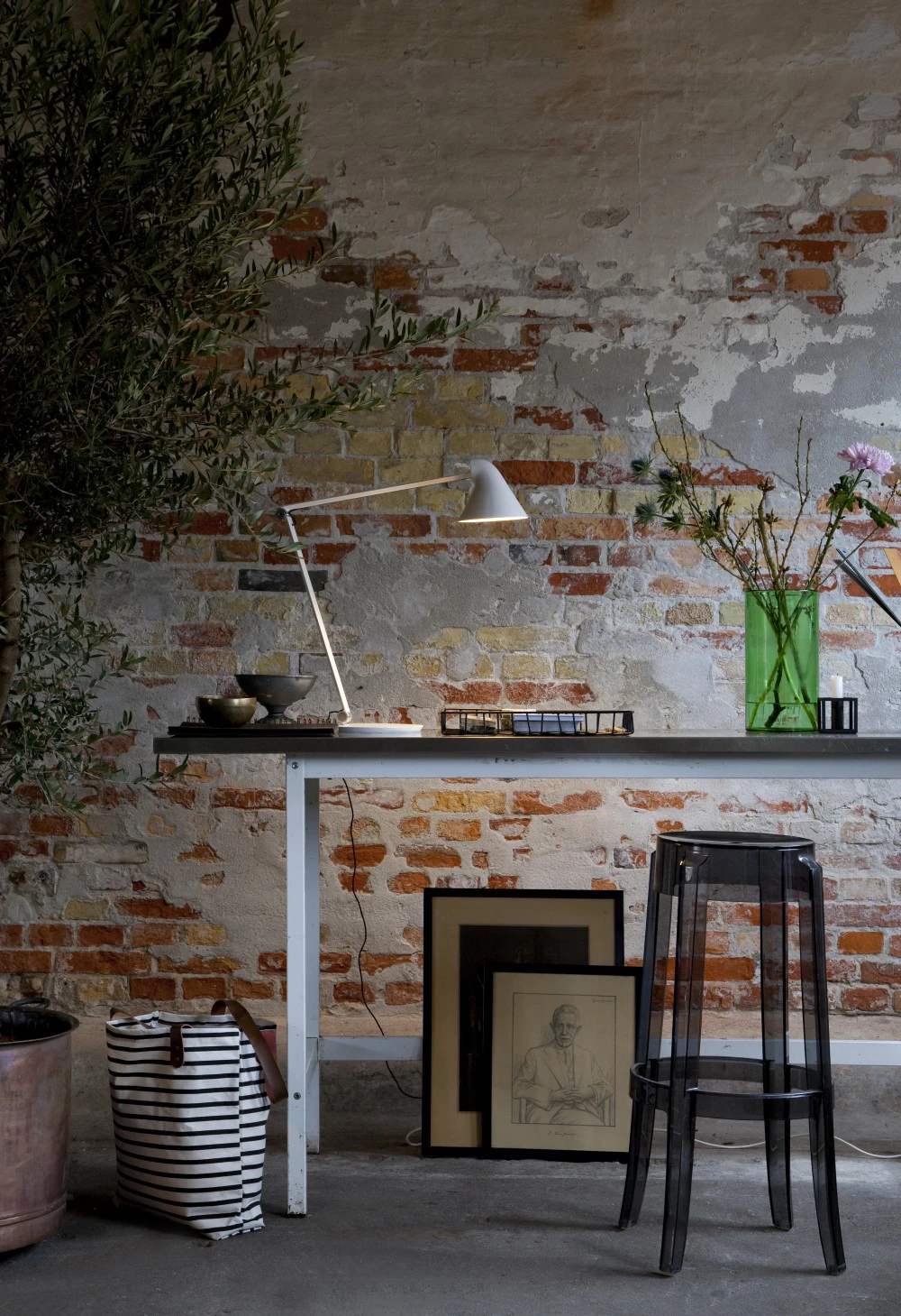 A white AJ Table Lamp stands on a table against a weathered brick wall with peeling plaster. © 2026 Louis Poulsen.