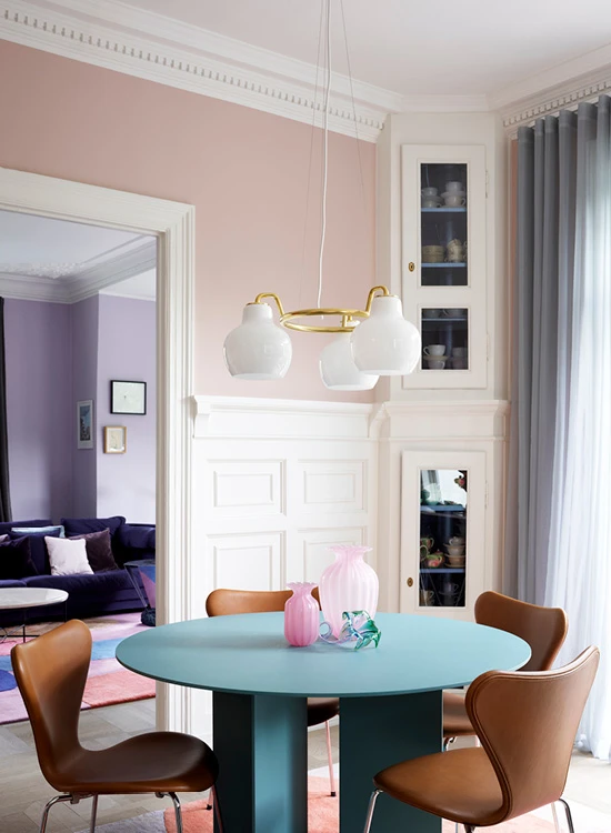 Eine VL Ring Crown 3-5-7 Pendelleuchte mit weißen Glasschirmen hängt über einem türkisfarbenen Esstisch in einem rosafarbenen Esszimmer. © 2026 Louis Poulsen.
