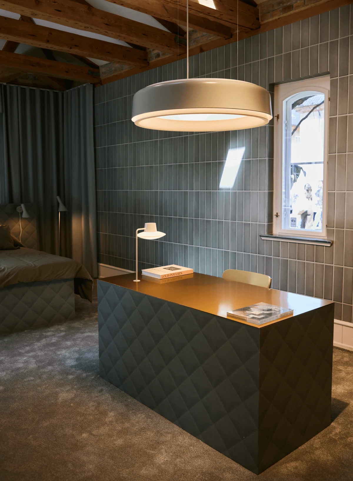 A LP Grand Suspended and an AJ Table Lamp illuminate a room with a desk, tiled walls and exposed timber beams. © 2026 Louis Poulsen.