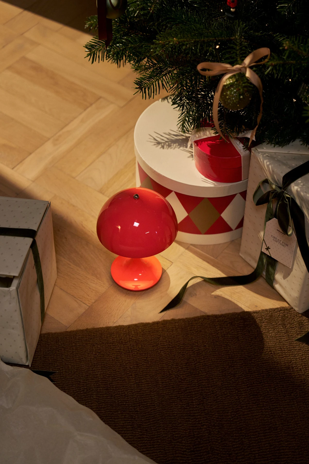 A red Panthella 160 Portable Lamp glows among wrapped presents beneath a Christmas tree. © 2026 Louis Poulsen.