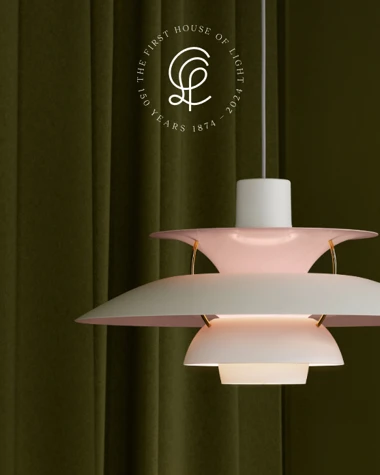 A PH 5 Anniversary Edition pendant in soft pink and white against dark green curtains. © 2026 Louis Poulsen.