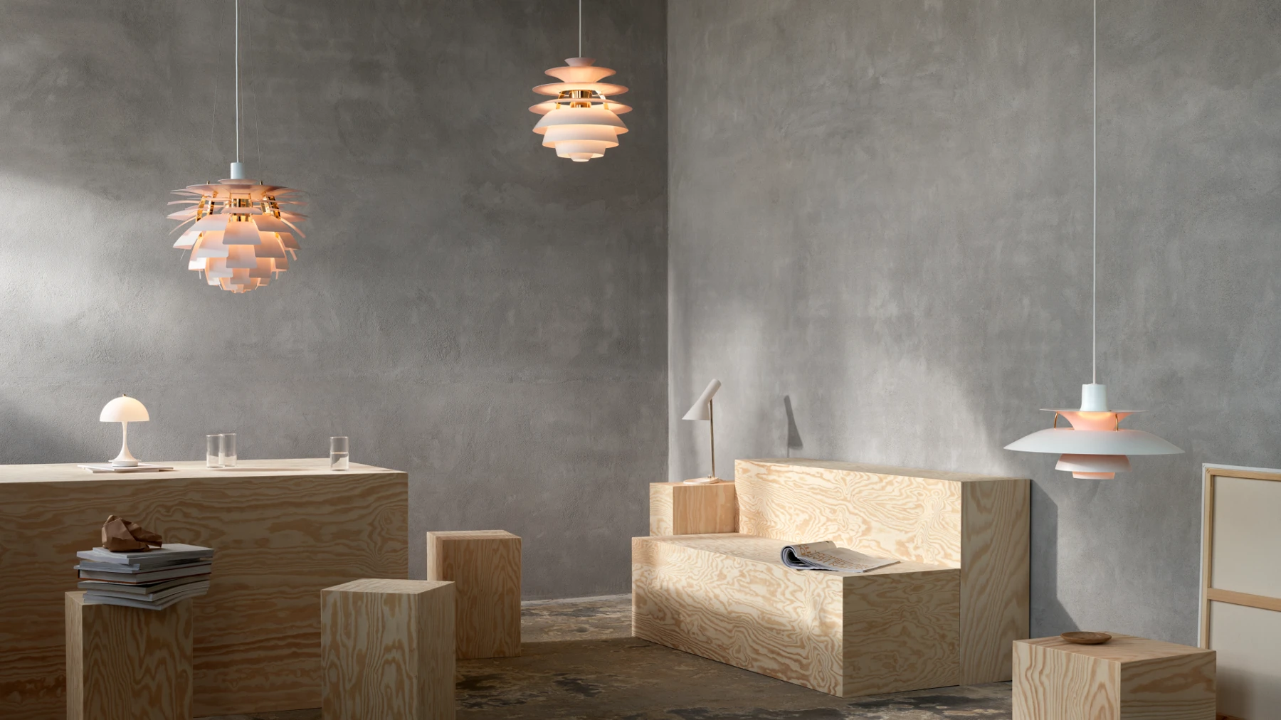 PH Artichoke, PH Snowball and PH 5 pendants illuminate pale plywood furniture against bare concrete walls. © 2026 Louis Poulsen.