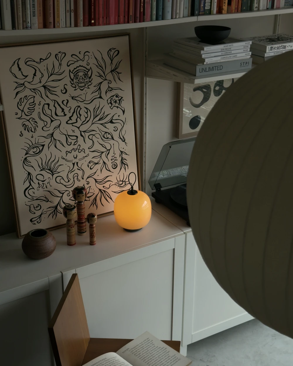 A VL 45 Radiohus Portable Table Lamp glowing next to art and wooden figurines on a white cabinet, © 2025 Louis Poulsen.