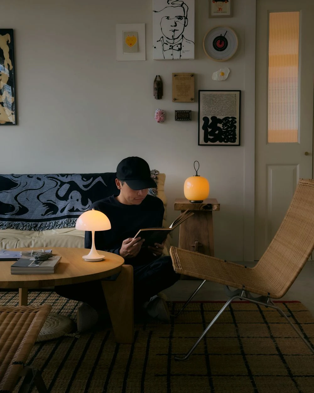 A man reading by a glowing Panthella Portable 160 and VL 45 Radiohus Portable Table Lamp on a wooden table in a cozy living room, © 2025 Louis Poulsen.