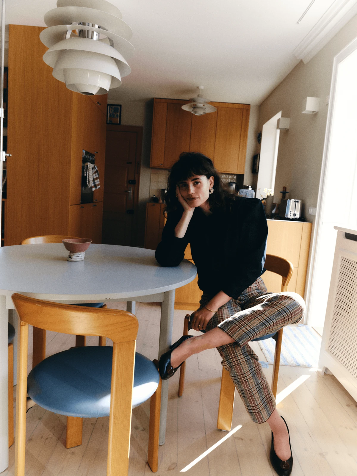 Portrait of Simone Noa seated beneath PH pendant lighting in home kitchen, © 2025 Louis Poulsen.