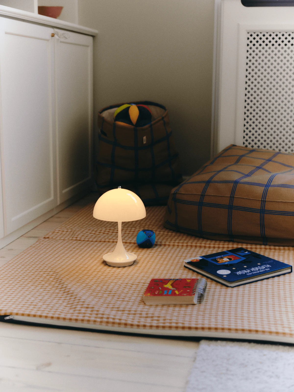 Panthella 160 Portable providing gentle light beside children’s books and cushions, © 2025 Louis Poulsen.
