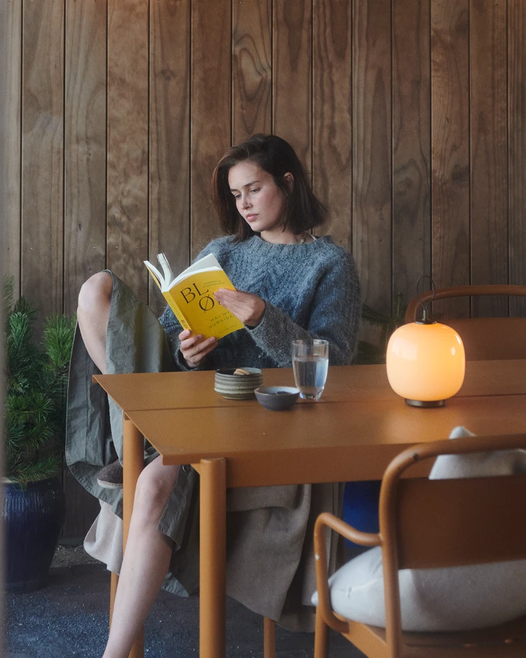 VL45 Portable lamp on dining table beside woman reading book, © 2025 Louis Poulsen.