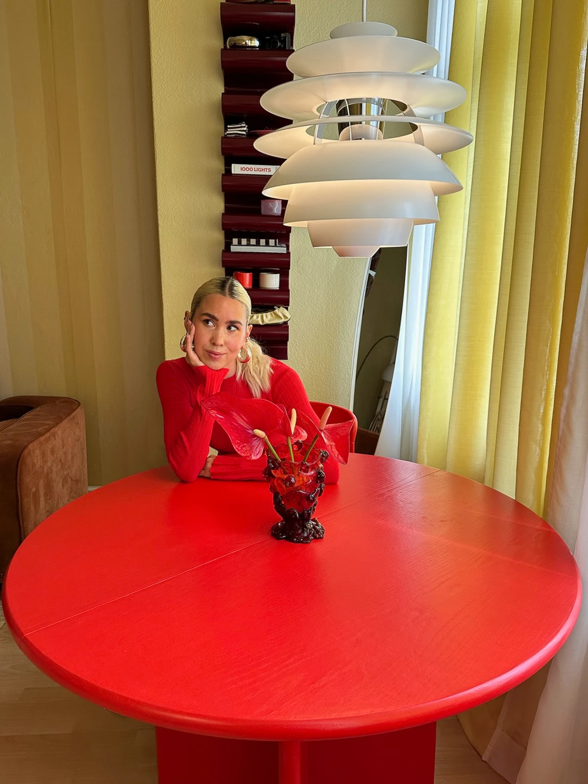 Sarah Hartmann seated under PH Snowball pendant at red dining table, © 2025 Louis Poulsen.