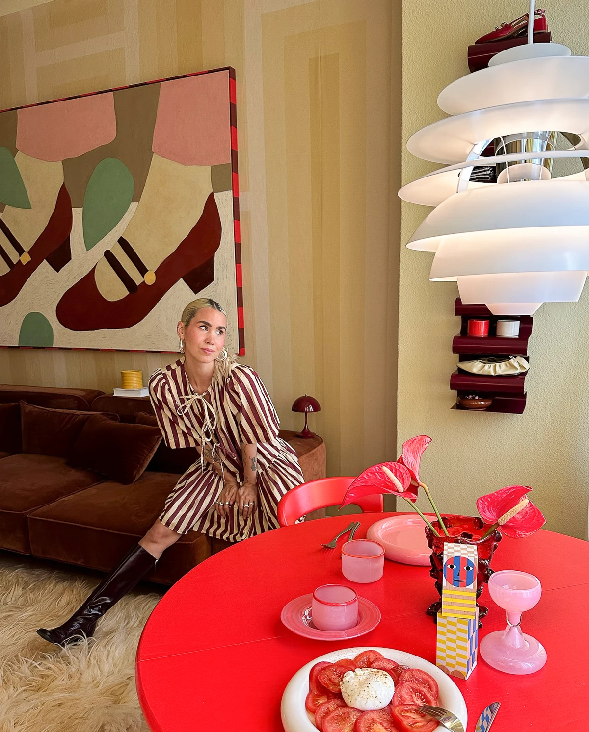 A white PH Louvre ceiling lamp hangs in a colourful living room with wall art and a red dining table. © 2026 Louis Poulsen.