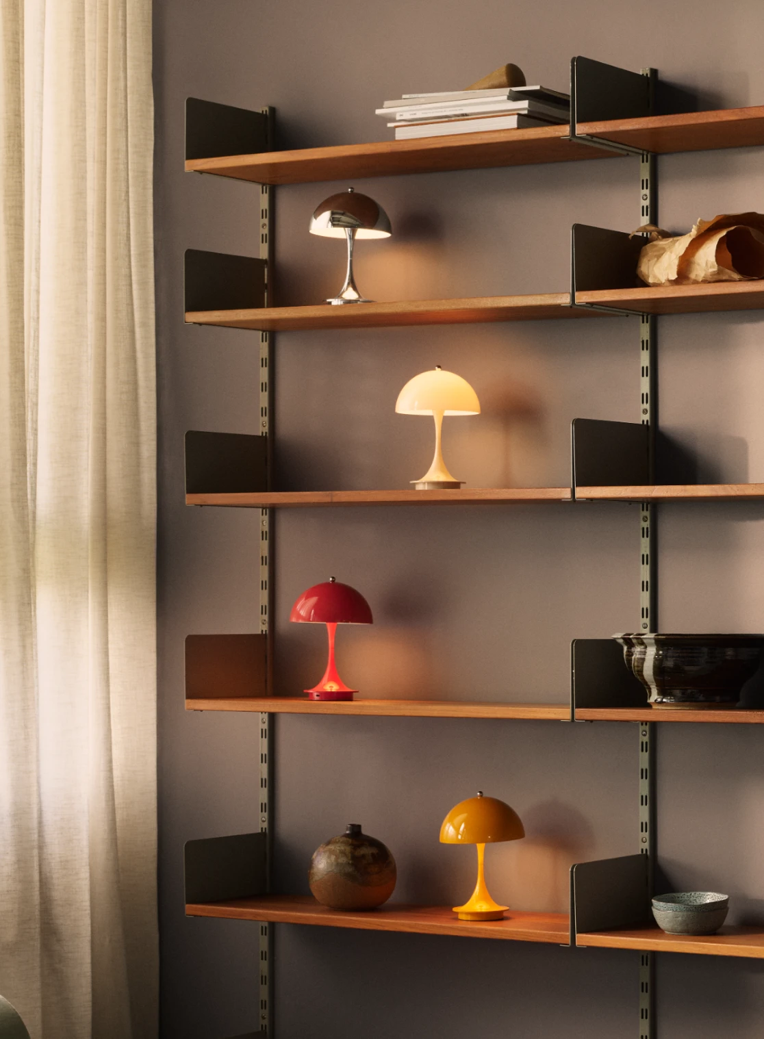 Vier Panthella 250 Portable Lamps in Chrom, Gelb, Rot und Orange stehen auf Holzregalen. © 2026 Louis Poulsen.