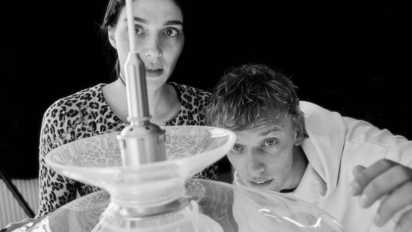 Two people examine a glass PH Septima pendant in a black-and-white portrait. © 2026 Louis Poulsen.