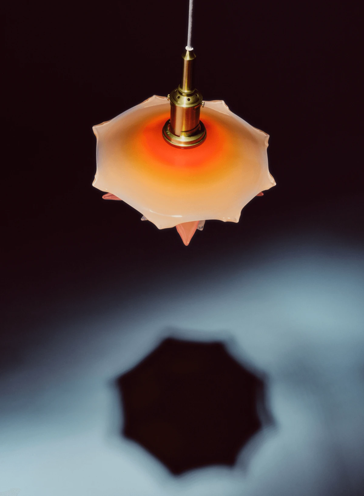 A PH Septima pendant in opal glass and brass glows warmly, casting a distinct shadow against the dark background. © 2026 Louis Poulsen.