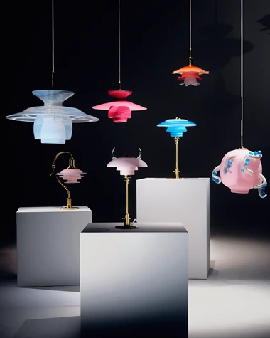 Colourful glass PH 5 pendants and table lamps are displayed on plinths against a dark backdrop. © 2026 Louis Poulsen.