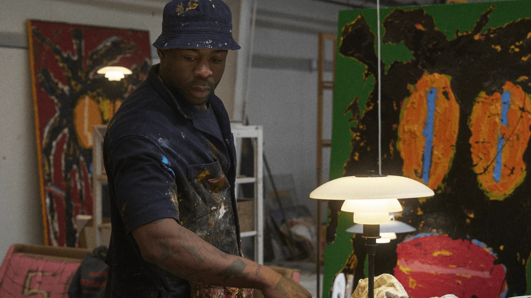 Jack Kabangu in his studio beside illuminated PH lamps and colourful paintings, © 2025 Louis Poulsen.