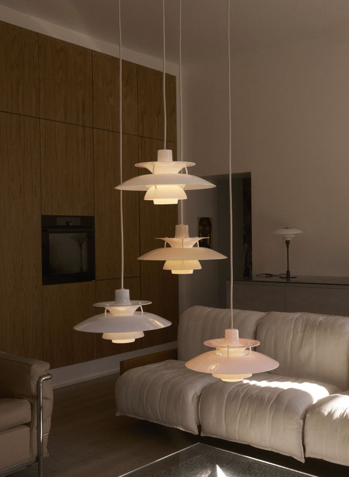 Four pale pink PH 5 pendants glow above a sofa in a living room with wood-panelled walls. © 2026 Louis Poulsen.