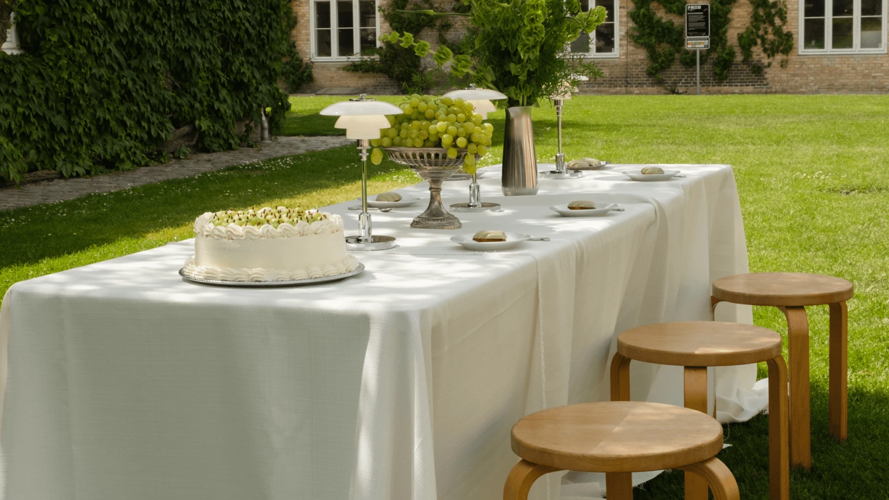 Une Panthella 250 Portable Lamp blanche sur une table dressée dans un jardin verdoyant. © 2026 Louis Poulsen.