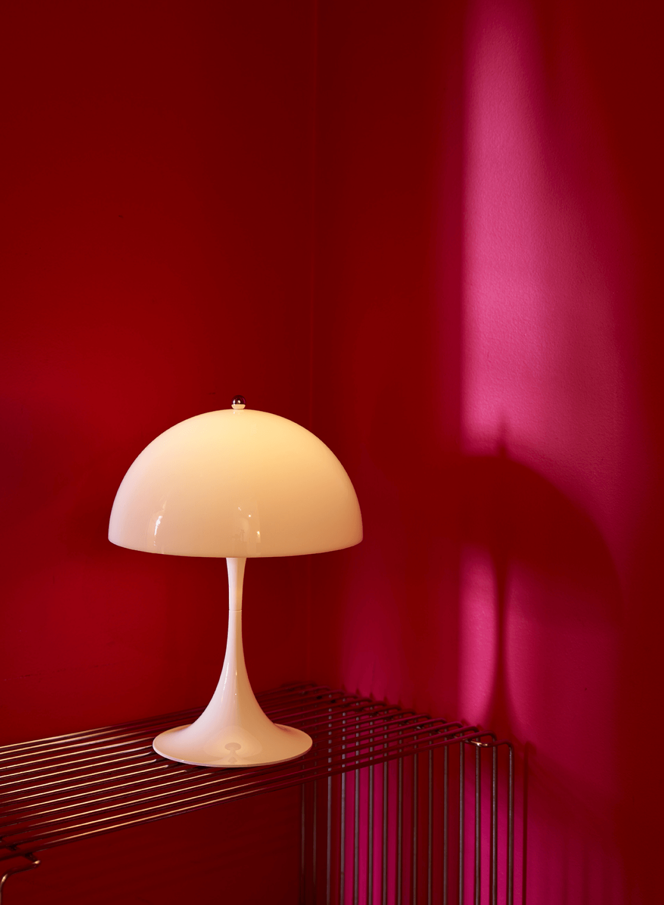 Panthella 250 Portable on a wire shelf against a red wall, © 2025 Louis Poulsen.