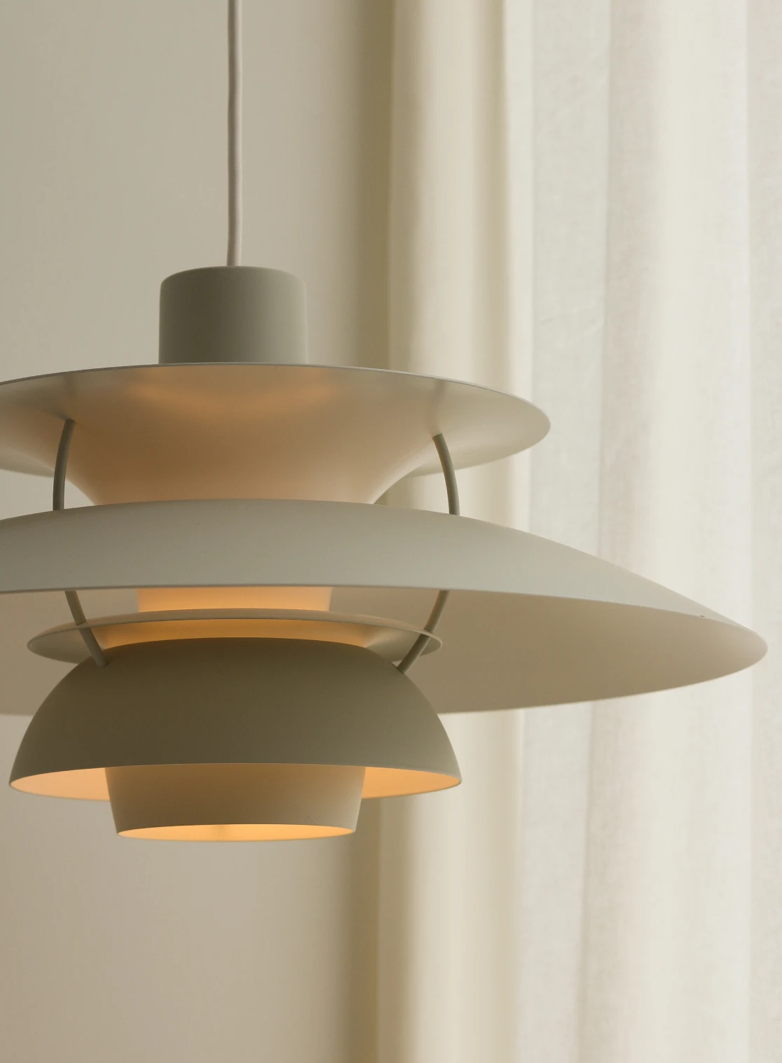 A white PH 5 pendant glows warmly in front of light curtains. © 2026 Louis Poulsen.