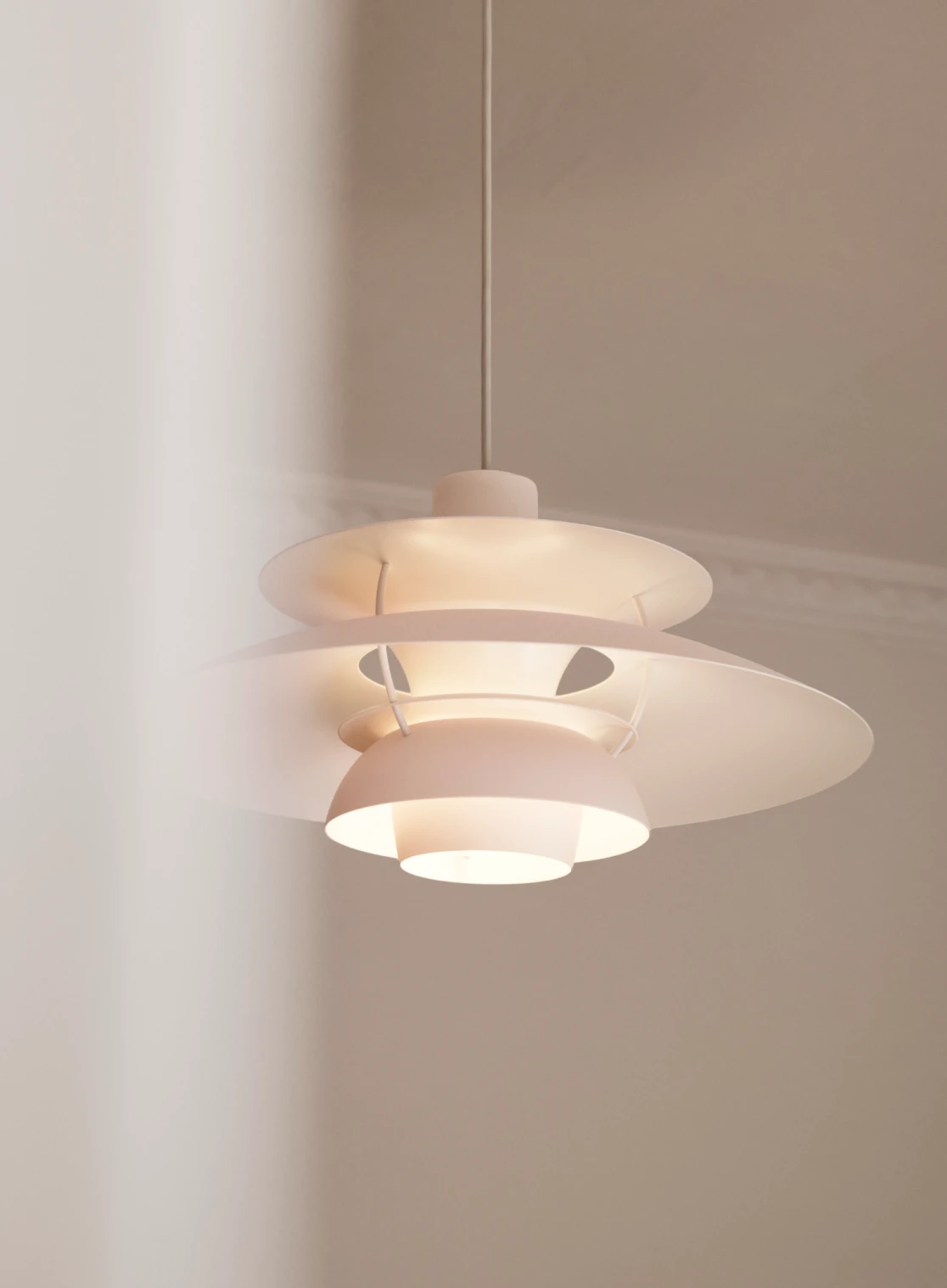 A white PH 5 pendant casts a warm glow in a calm, neutral-toned room. © 2026 Louis Poulsen.