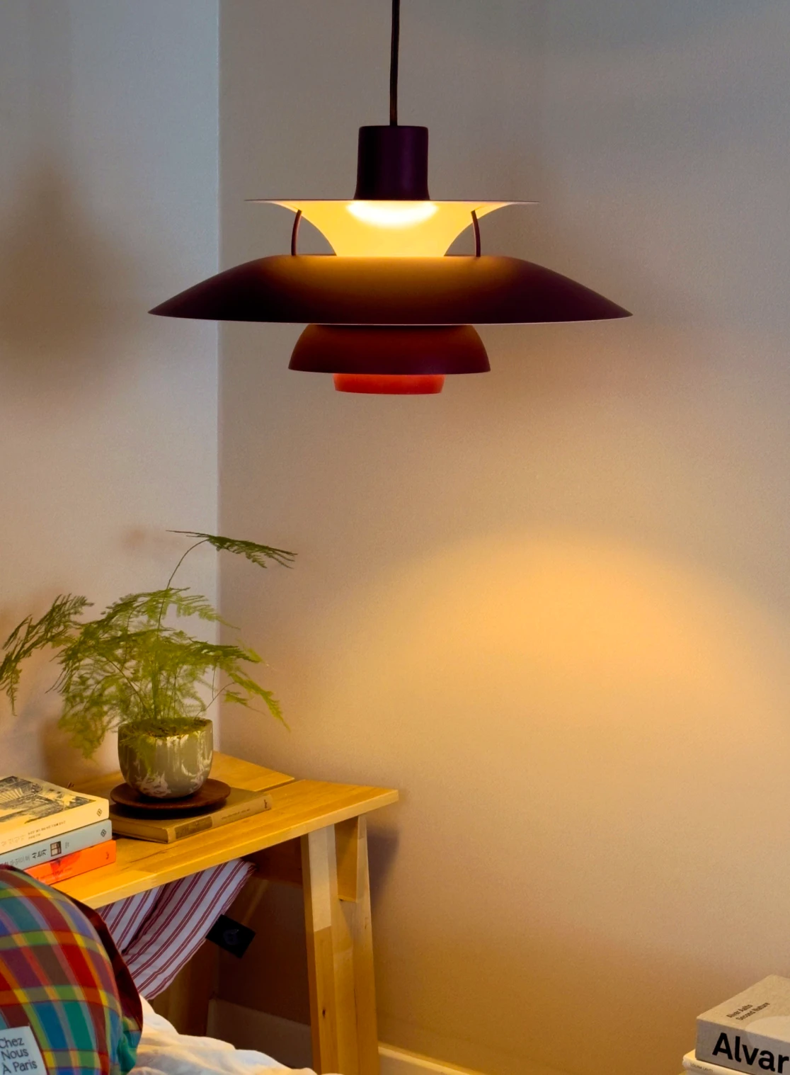A dark red PH 5 pendant casts warm light beside a small wooden table with a potted fern. © 2026 Louis Poulsen.