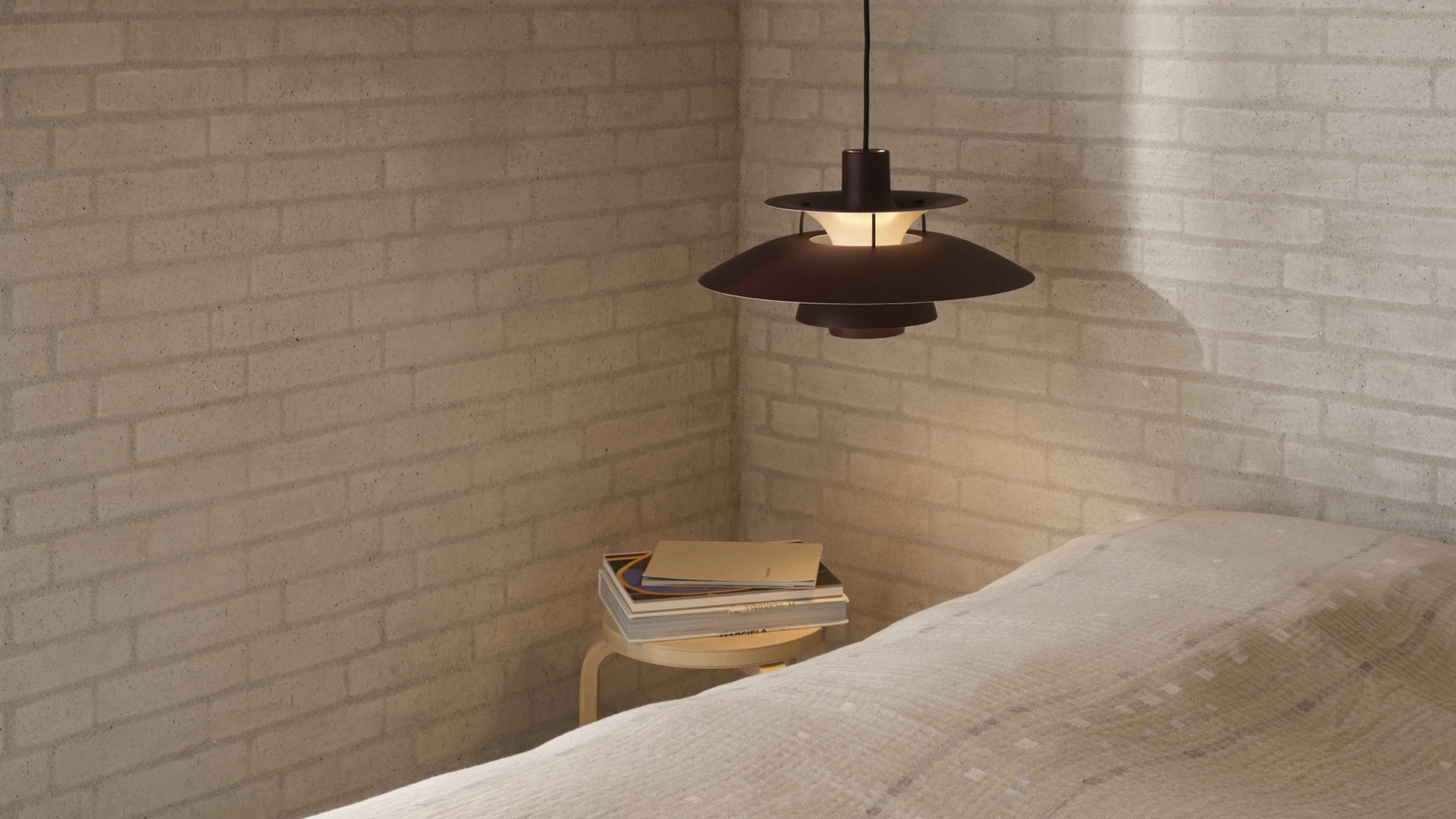 A dark PH 5 pendant casts a warm glow in a bedroom with a brick wall and a bedside table. © 2026 Louis Poulsen.