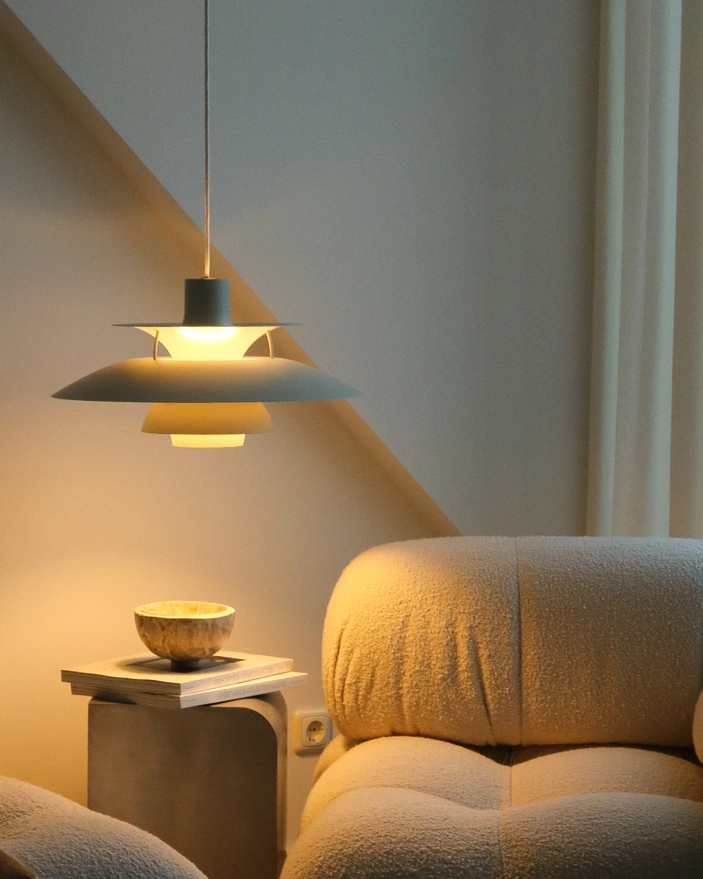A dark green PH 5 pendant casts a warm glow beside a soft armchair and small side table. © 2026 Louis Poulsen.