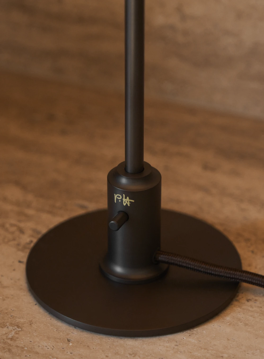 The dark metal base and stem of a PH 2/1 Table Lamp, with a signature detail, rest on warm-toned stone. © 2026 Louis Poulsen.