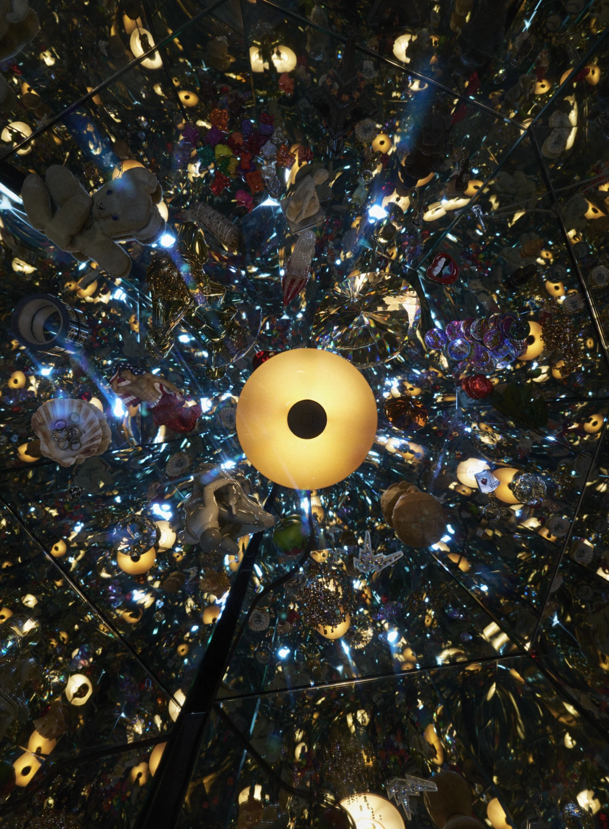 A PH 2/1 Pendant glows warmly in a mirrored room filled with reflections of colourful objects. © 2026 Louis Poulsen.