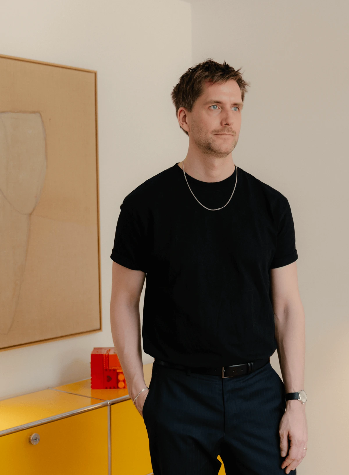 Sigurd Larsen standing by a yellow cabinet with artwork in background, © 2025 Louis Poulsen.