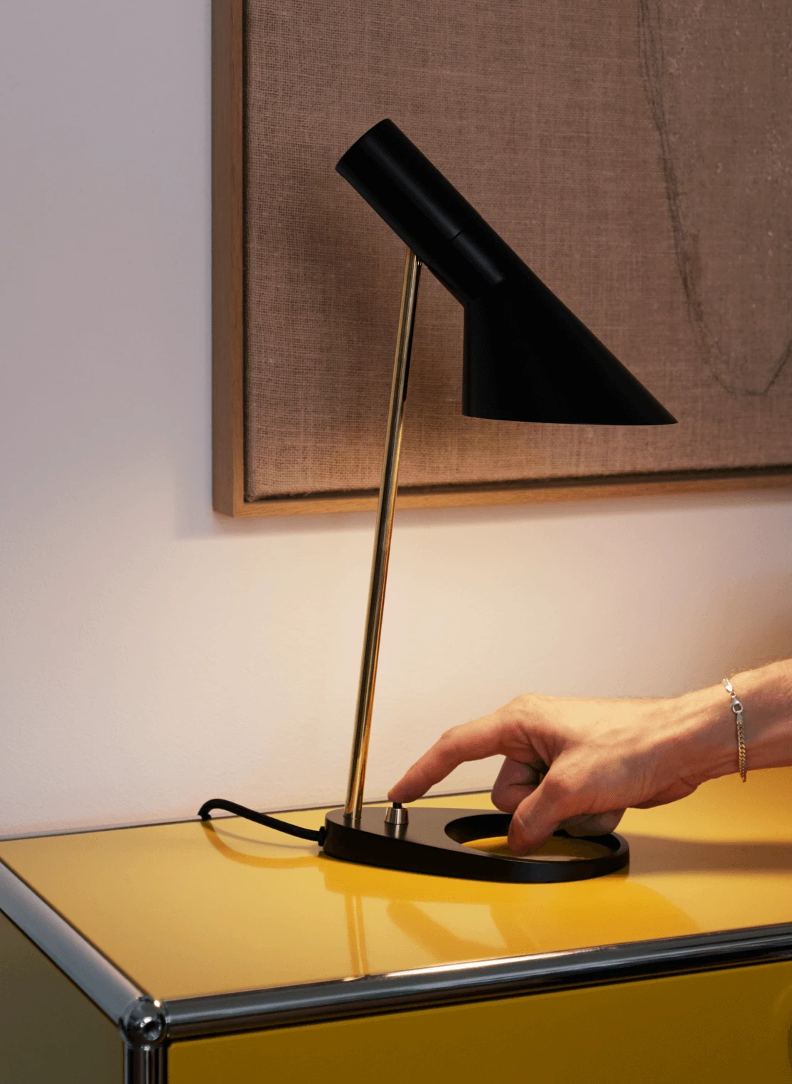 AJ Table lamp being switched on, placed on a yellow cabinet, © 2025 Louis Poulsen.