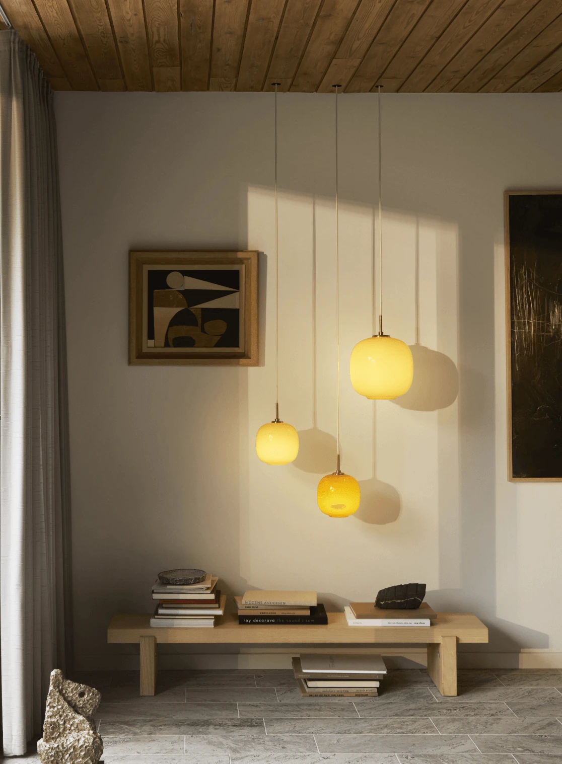 Drei Moser Pendant-Pendelleuchten aus gelbem und bernsteinfarbenem Glas hängen über einer niedrigen Bank. © 2026 Louis Poulsen.