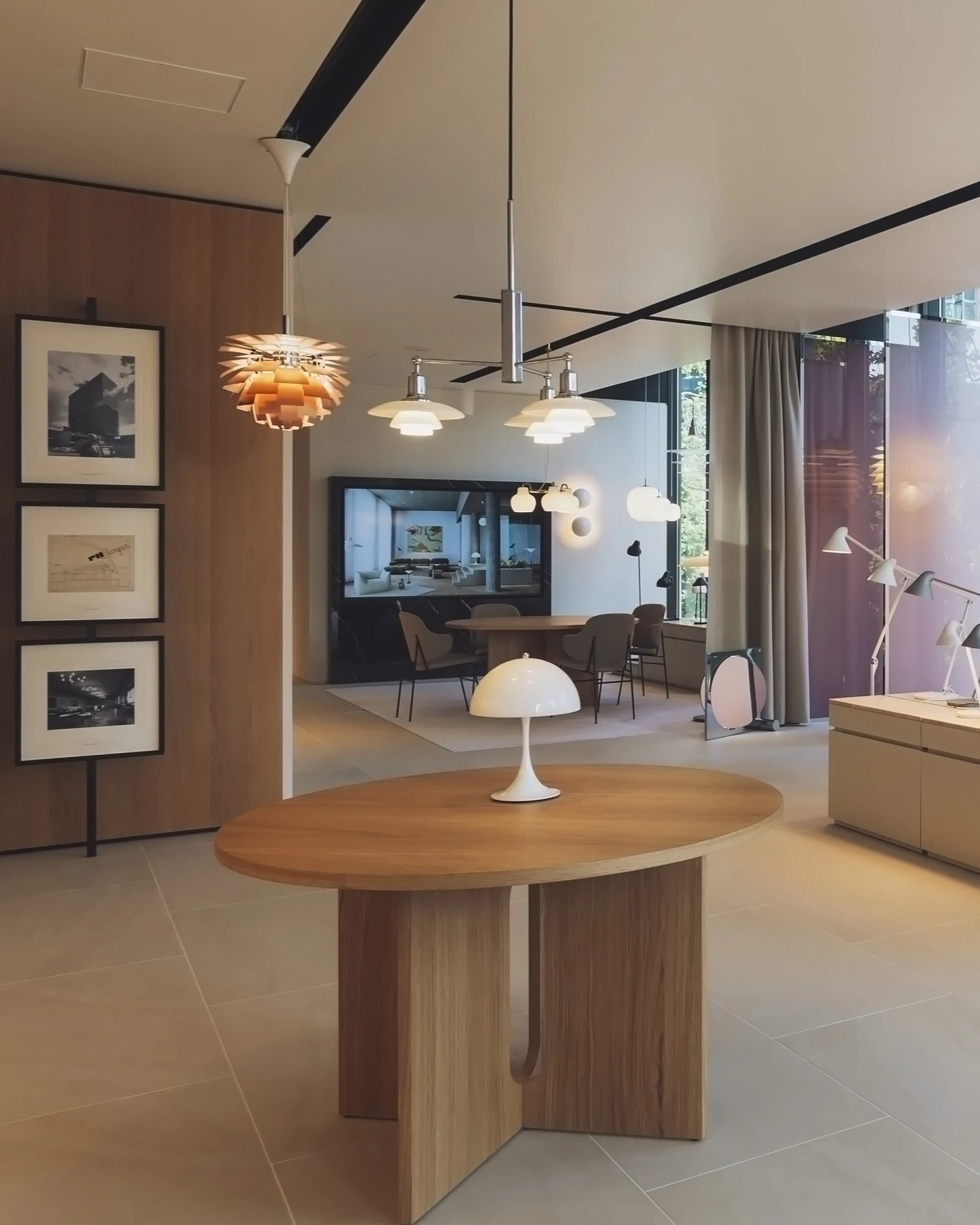 白いPanthella 250 Table Lampが、PH Artichokeのペンダントが見えるルイスポールセン東京ショールームの丸い木製テーブルに置かれています。 © 2026 Louis Poulsen.
