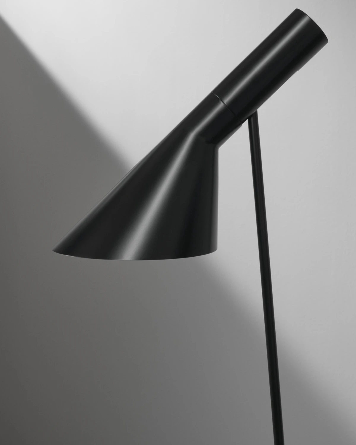 Zwarte AJ Floor vloerlamp van dichtbij tegen een grijze muur. © 2026 Louis Poulsen.