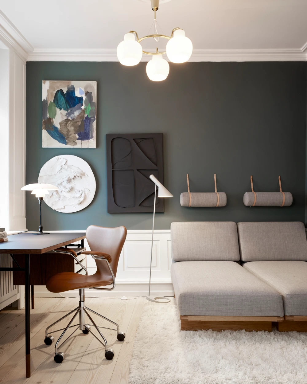 Een witte AJ Floor Lamp en een PH 3/2 tafellamp in een lichte woonkamer met een donkergroene muur en een grijze bank. © 2026 Louis Poulsen.