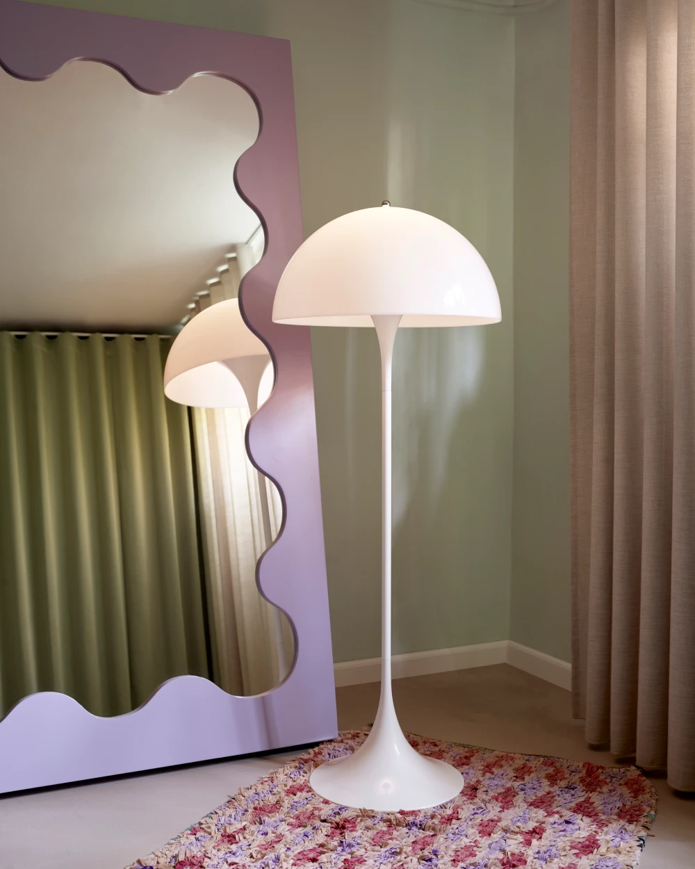 A white Panthella Floor Lamp stands on a colourful rug beside a wavy mirror and floor-length curtains. © 2026 Louis Poulsen.