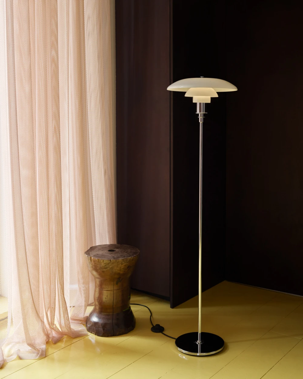 A PH 3½-2½ Floor Lamp with white shades and a chrome stem beside a wooden stool on a yellow floor. © 2026 Louis Poulsen.