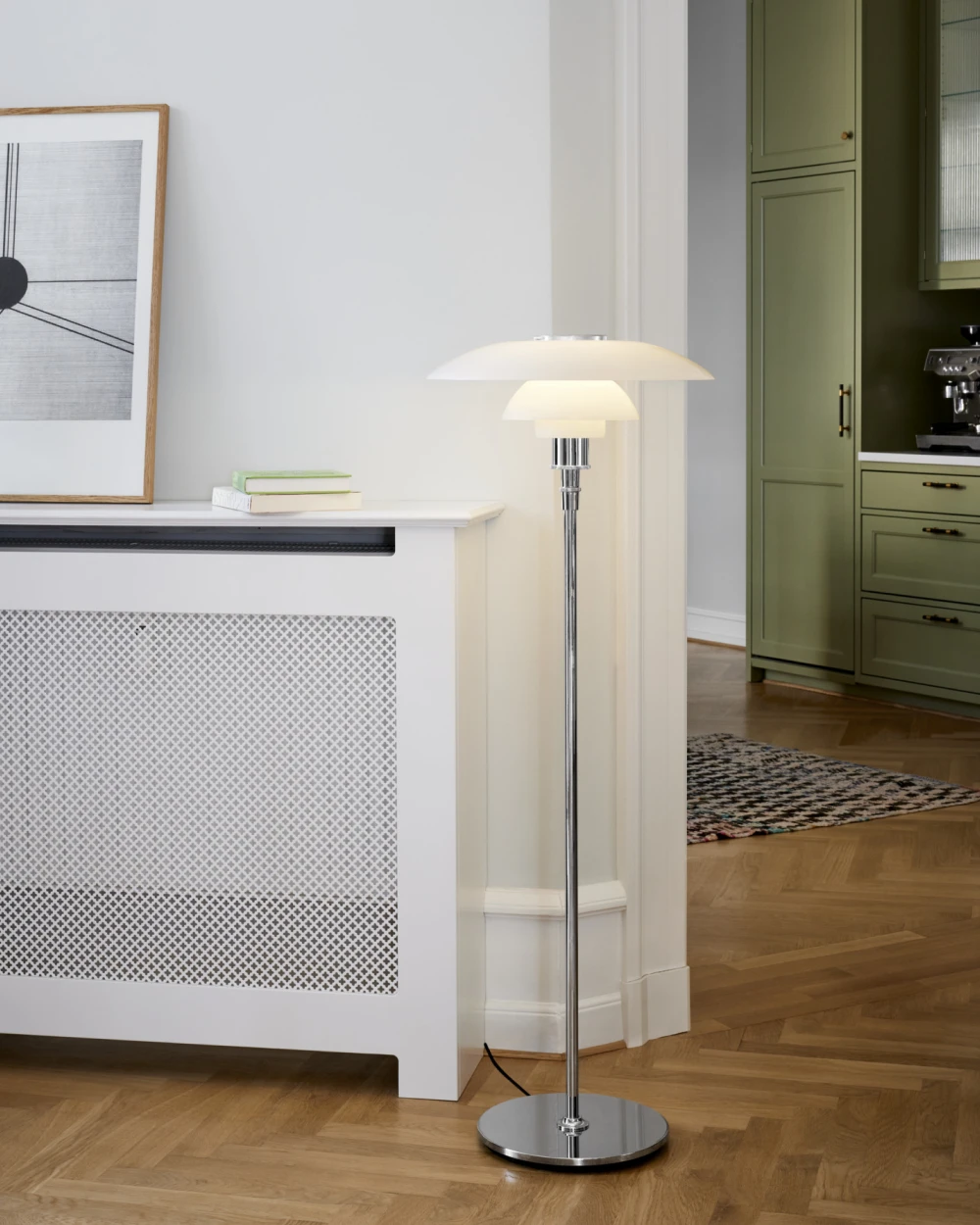 A PH 4½-3½ Floor Lamp with white shades and a chrome stem stands beside a radiator cover on a parquet floor. © 2026 Louis Poulsen.