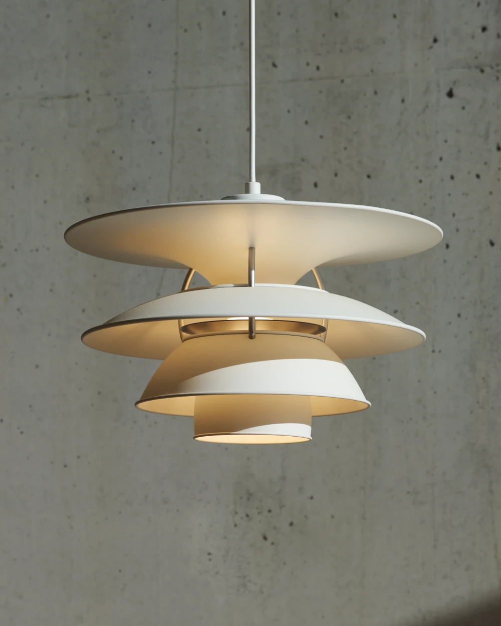 A white PH 5-4½ & PH 6½-6 pendant glows warmly against a raw concrete wall. © 2026 Louis Poulsen.