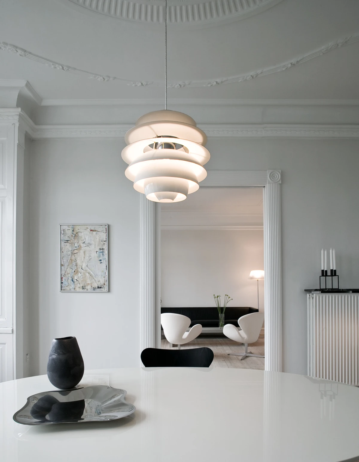A white PH Snowball pendant lights a round dining table in a bright room with ornate plasterwork. © 2026 Louis Poulsen.