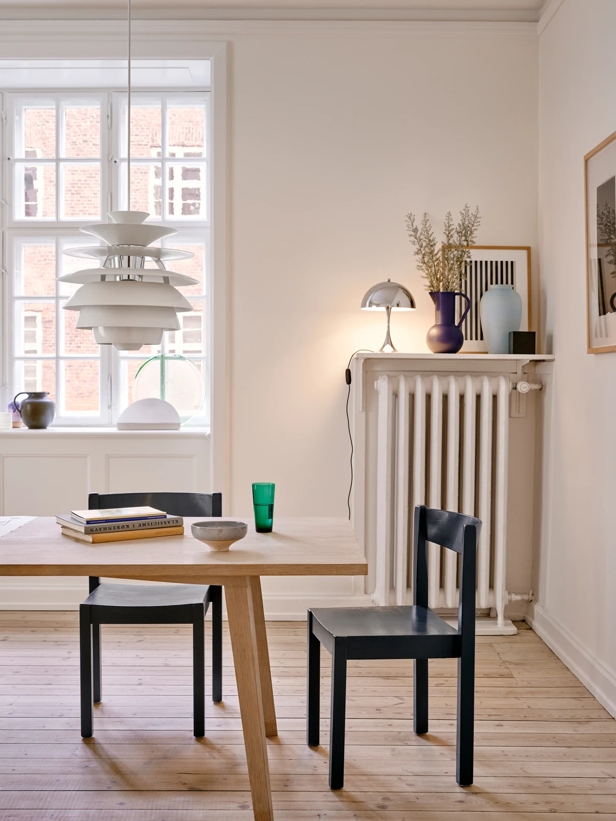A white PH Snowball pendant hangs above a light wood dining table in a bright room. © 2026 Louis Poulsen.