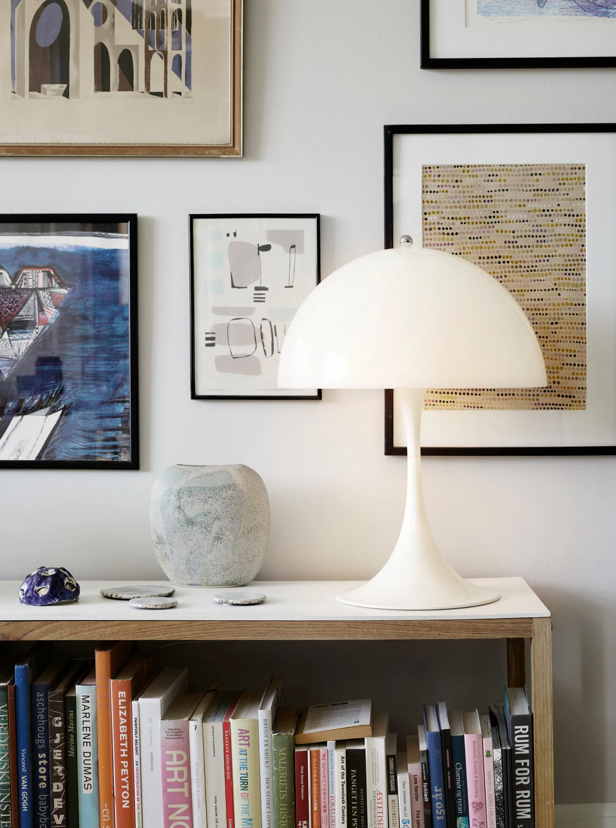 A white Panthella 400 Table Lamp on a bookcase beneath framed artwork in an apartment. © 2026 Louis Poulsen.