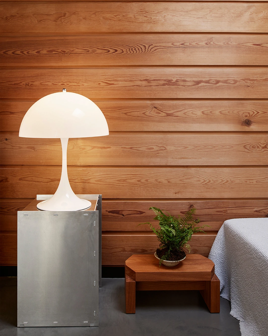 A white Panthella 400 Table Lamp stands on a metal cabinet against a wall of warm wooden planks. © 2026 Louis Poulsen.