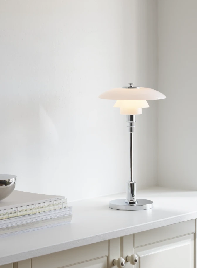 A PH 2/1 Portable Lamp in opal white glass and chrome sits on a white cabinet. © 2026 Louis Poulsen.