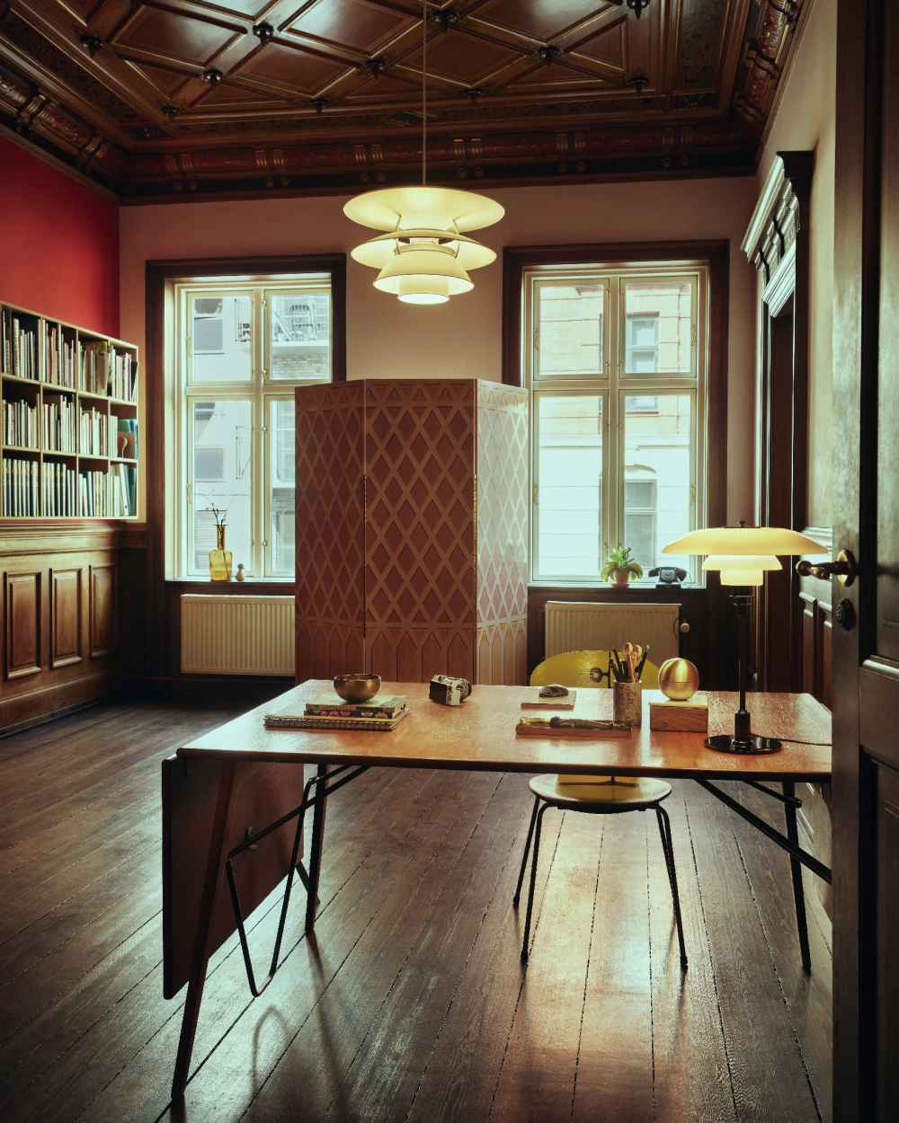A white PH 5 pendant and a PH 4/3 Table Lamp illuminate a study with red walls, wood panelling and a carved ceiling. © 2026 Louis Poulsen.